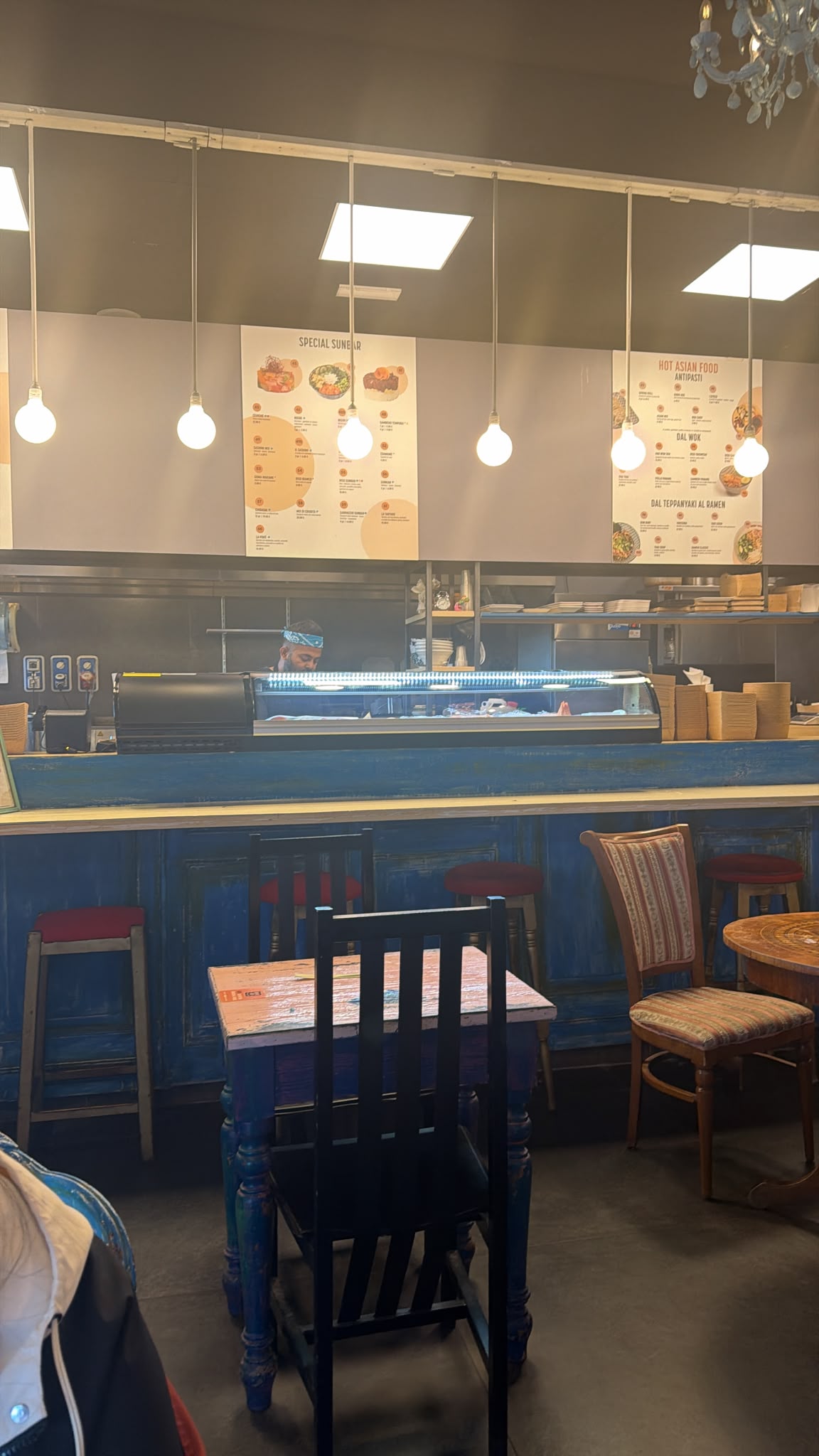 Il locale: bancone blu, tavoli in legno, sedute vintage e luci sospese
